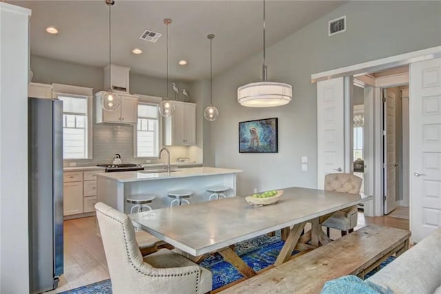 kitchen featuring a kitchen breakfast bar, light hardwood / wood-style flooring, stainless steel fridge, pendant lighting, and a center island with sink