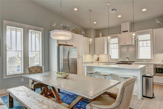 kitchen with pendant lighting, a healthy amount of sunlight, stainless steel appliances, and an island with sink