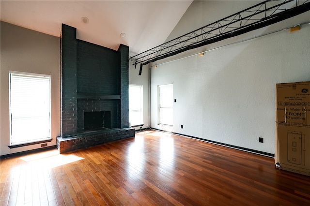 unfurnished living room featuring hardwood / wood-style floors, high vaulted ceiling, and a brick fireplace