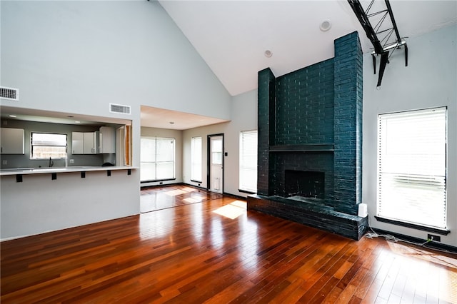 unfurnished living room with high vaulted ceiling, hardwood / wood-style floors, a healthy amount of sunlight, and a fireplace