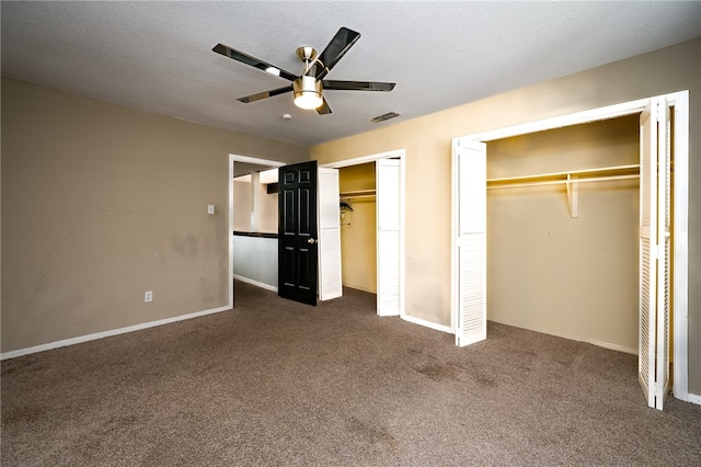 unfurnished bedroom with a textured ceiling, ceiling fan, dark carpet, and two closets