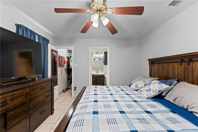 tiled bedroom featuring a walk in closet, ensuite bath, ceiling fan, sink, and a closet