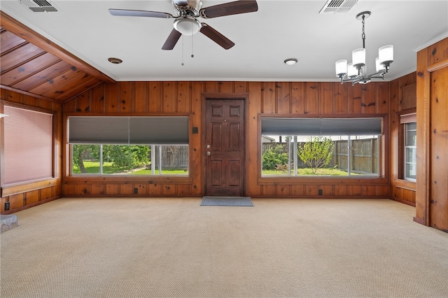 unfurnished living room with wooden walls, vaulted ceiling, light carpet, and ceiling fan with notable chandelier