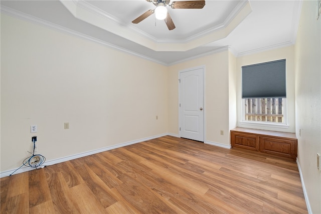 empty room featuring light wood-type flooring, ceiling fan, ornamental molding, and a raised ceiling