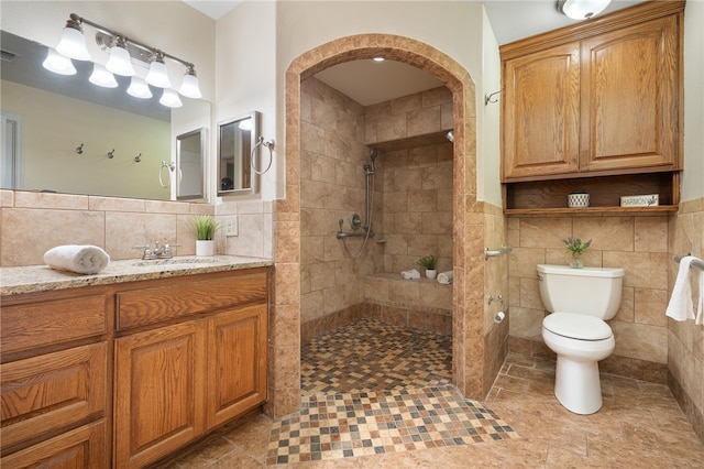 bathroom featuring tile walls, toilet, vanity, and a tile shower