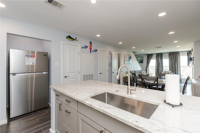 kitchen featuring light stone counters, wood finish floors, visible vents, freestanding refrigerator, and a sink