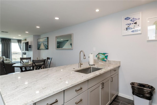 kitchen featuring visible vents, dark wood-type flooring, a sink, light stone countertops, and a peninsula