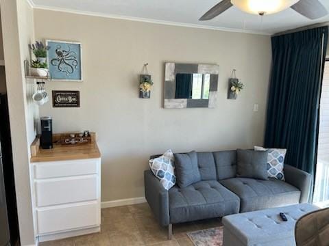 living area with ceiling fan, baseboards, and crown molding