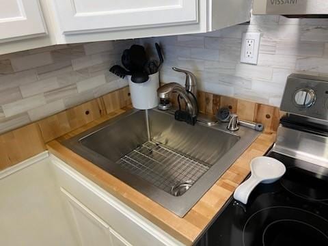 interior details with a sink, wooden counters, backsplash, and white cabinetry