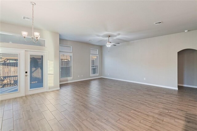 unfurnished living room with ceiling fan with notable chandelier and light hardwood / wood-style flooring