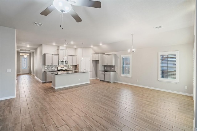 kitchen with light hardwood / wood-style flooring, stainless steel appliances, tasteful backsplash, a center island with sink, and decorative light fixtures