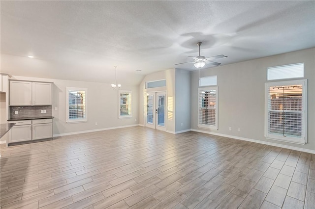 unfurnished living room featuring ceiling fan with notable chandelier, a wealth of natural light, a textured ceiling, and light wood-type flooring