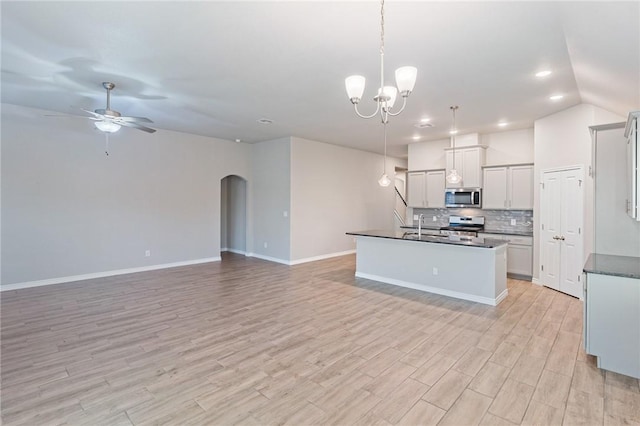 kitchen with decorative light fixtures, a center island with sink, stainless steel appliances, ceiling fan with notable chandelier, and backsplash