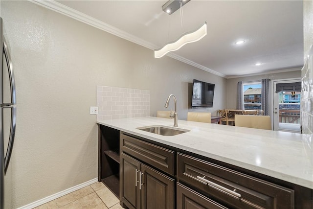 kitchen with dark brown cabinets, ornamental molding, freestanding refrigerator, and a sink