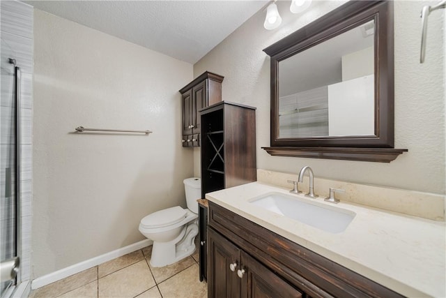 bathroom with toilet, a shower with door, tile patterned flooring, baseboards, and vanity