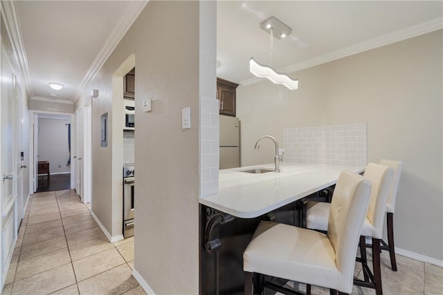 kitchen with a breakfast bar, a sink, freestanding refrigerator, crown molding, and light tile patterned floors