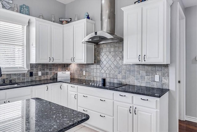 kitchen featuring black electric cooktop, dark stone counters, wall chimney exhaust hood, and white cabinetry