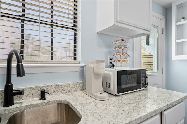 room details featuring light stone counters, stainless steel microwave, white cabinets, and a sink