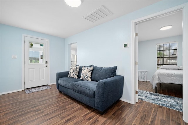 living room with dark wood-style flooring, visible vents, and baseboards