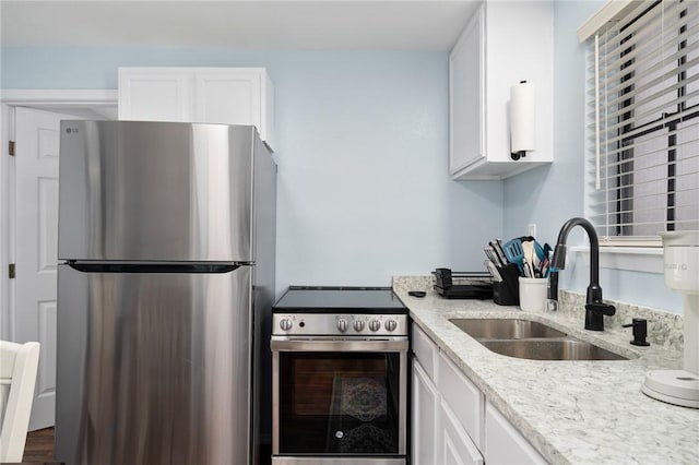 kitchen featuring stainless steel appliances, light stone counters, a sink, and white cabinetry