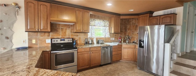 13757 Cayo Gorda Ct, Corpus Christi, TX 78418 - kitchen with stainless steel appliances, light stone counters, backsplash, brown cabinetry, and a peninsula