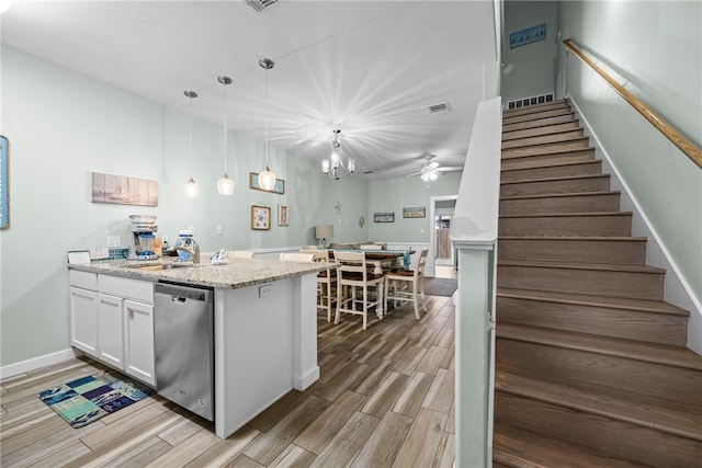 kitchen featuring light stone counters, light wood-type flooring, stainless steel dishwasher, white cabinets, and pendant lighting