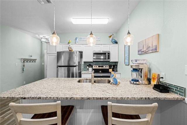 kitchen featuring a breakfast bar, appliances with stainless steel finishes, decorative light fixtures, white cabinets, and decorative backsplash