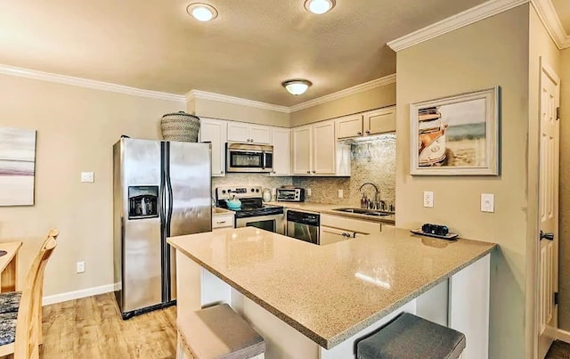 kitchen with a sink, light stone counters, tasteful backsplash, appliances with stainless steel finishes, and a peninsula