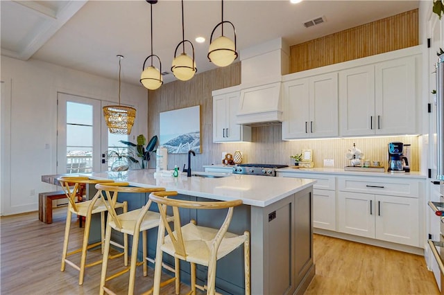 kitchen with pendant lighting, sink, a kitchen island with sink, custom range hood, and white cabinets