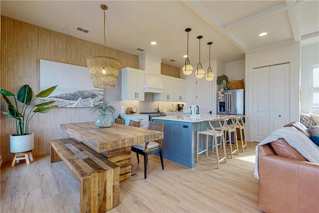 kitchen with appliances with stainless steel finishes, a kitchen breakfast bar, white cabinets, a center island with sink, and decorative light fixtures