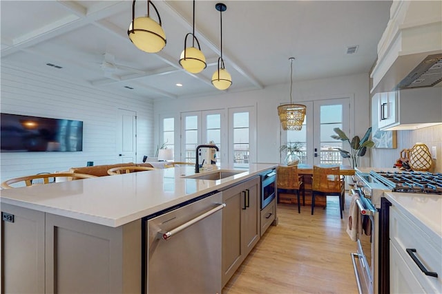 kitchen featuring sink, stainless steel appliances, custom range hood, a center island with sink, and french doors