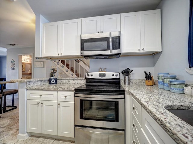 kitchen featuring light tile patterned flooring, appliances with stainless steel finishes, light stone countertops, and white cabinets