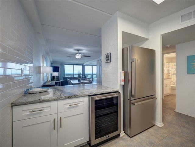 kitchen featuring stainless steel refrigerator, white cabinetry, wine cooler, light stone counters, and ceiling fan