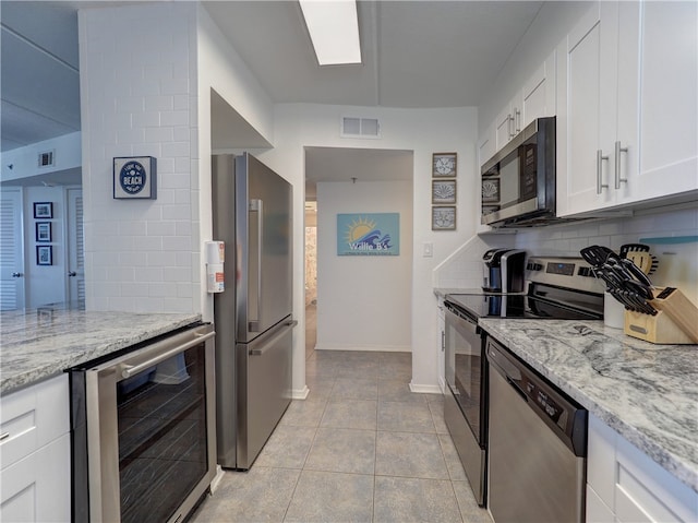 kitchen featuring stainless steel appliances, wine cooler, light stone counters, light tile patterned floors, and white cabinets