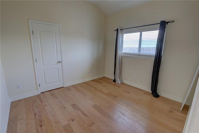 spare room with light wood-style floors, vaulted ceiling, and baseboards