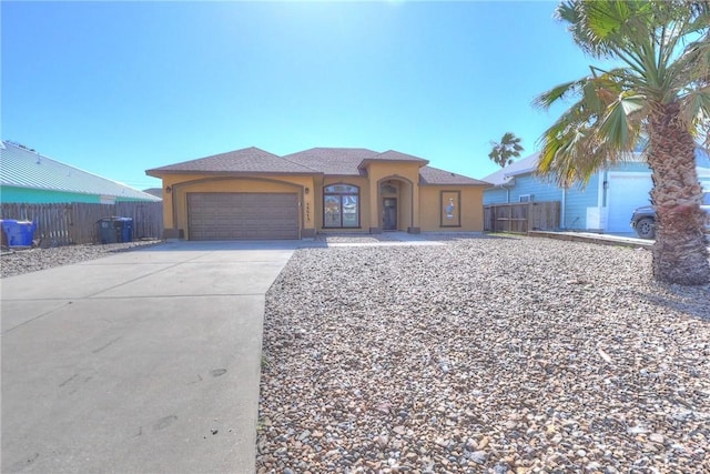 view of front facade with a garage, driveway, stucco siding, and fence