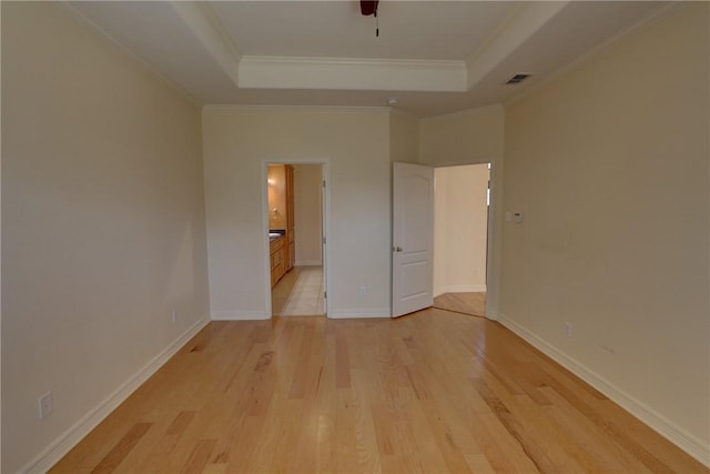 unfurnished bedroom with light wood-type flooring, a tray ceiling, crown molding, connected bathroom, and baseboards
