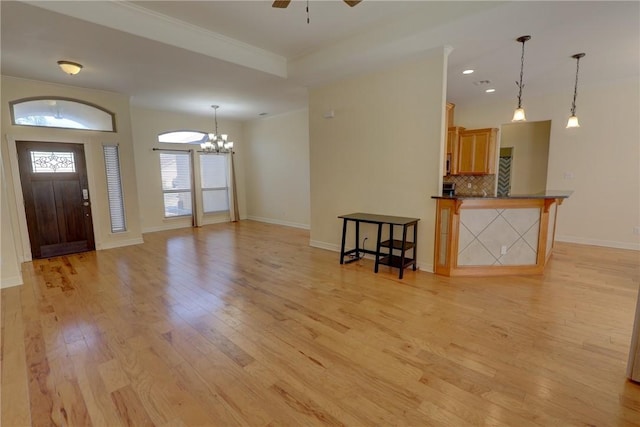 unfurnished living room featuring light wood-style floors, a chandelier, baseboards, ceiling fan, and ornamental molding