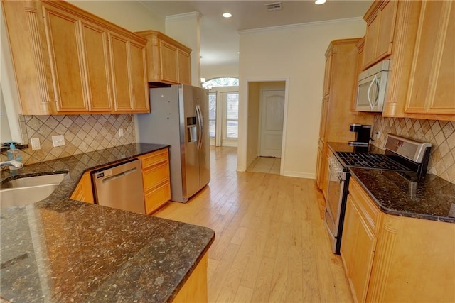 kitchen with appliances with stainless steel finishes, a sink, light wood finished floors, baseboards, and backsplash