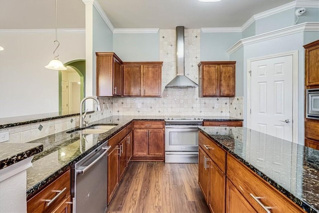 kitchen featuring wall chimney exhaust hood, sink, dark stone counters, pendant lighting, and stainless steel appliances