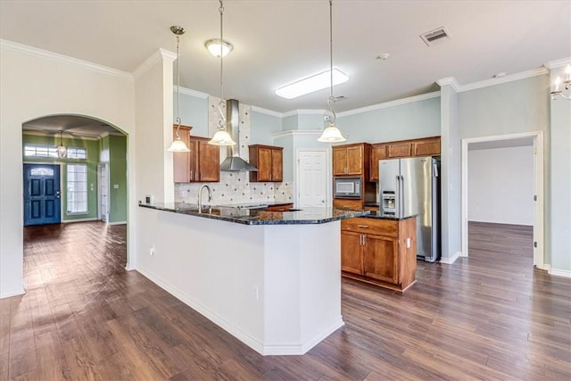 kitchen featuring pendant lighting, high end fridge, dark stone countertops, black microwave, and wall chimney exhaust hood