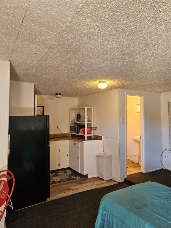 bedroom featuring a textured ceiling, black fridge, dark hardwood / wood-style flooring, and connected bathroom