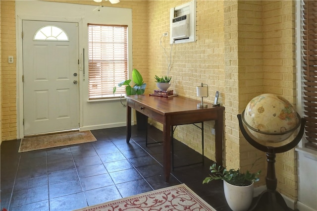 entrance foyer featuring brick wall, dark tile patterned flooring, ceiling fan, and a wall mounted air conditioner