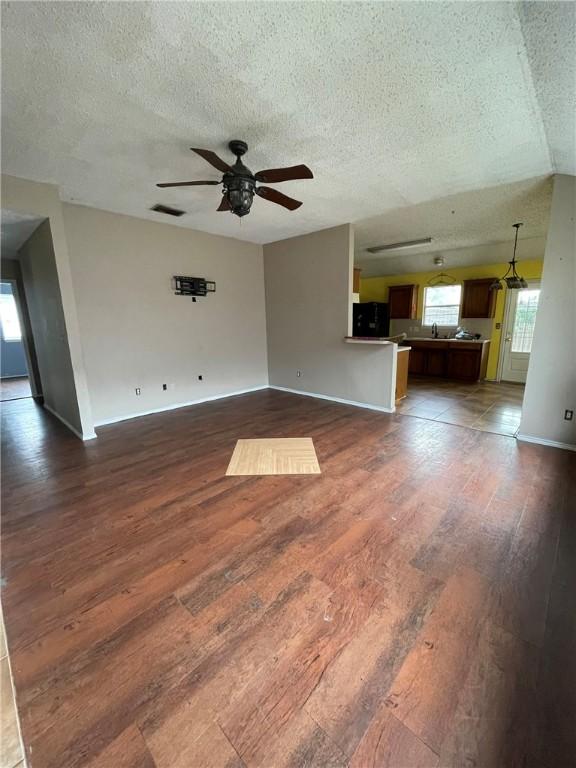 unfurnished living room featuring a textured ceiling, dark hardwood / wood-style floors, and ceiling fan