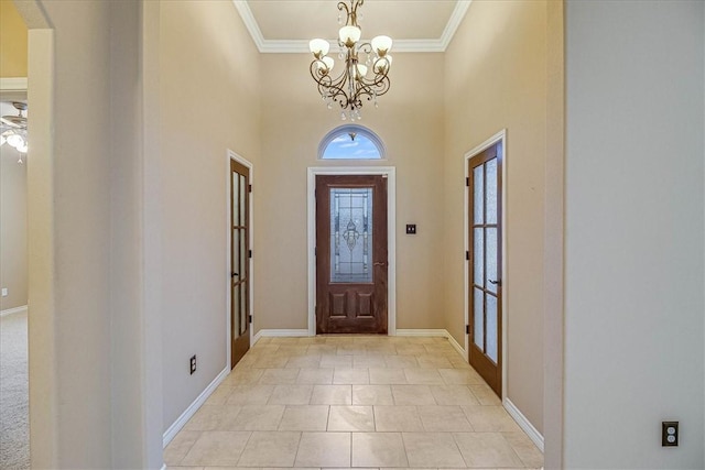 tiled foyer entrance with crown molding, a towering ceiling, and a notable chandelier