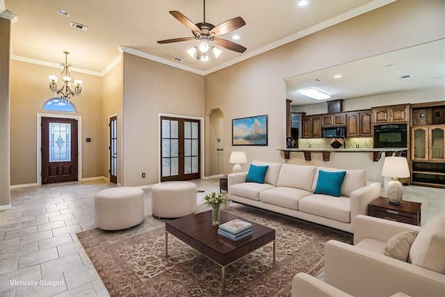 living room featuring french doors, light tile patterned floors, ornamental molding, ceiling fan with notable chandelier, and a high ceiling