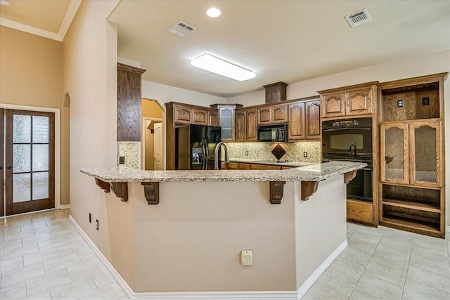 kitchen featuring light stone countertops, a breakfast bar, kitchen peninsula, and black appliances