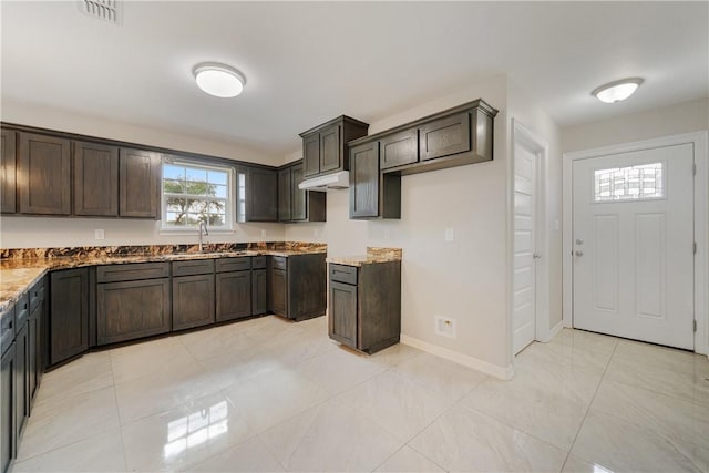 kitchen featuring light stone countertops, dark brown cabinetry, visible vents, a sink, and baseboards