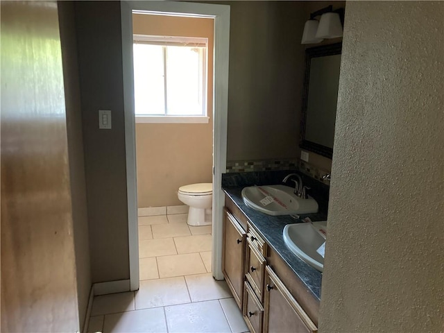 full bath featuring toilet, double vanity, tile patterned floors, and a sink