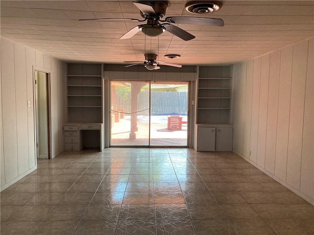 unfurnished living room featuring wooden walls, dark tile patterned floors, ceiling fan, and built in shelves